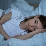 Una niña que cumple con los requisitos de sueño en una cama.