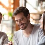 Four people are sitting together, smiling and laughing, in a bright indoor setting.