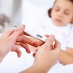 En el suroeste de Houston, una mujer sostiene con cuidado un termómetro frente a un niño en la cama, controlando su temperatura en busca de signos de fiebre infantil.