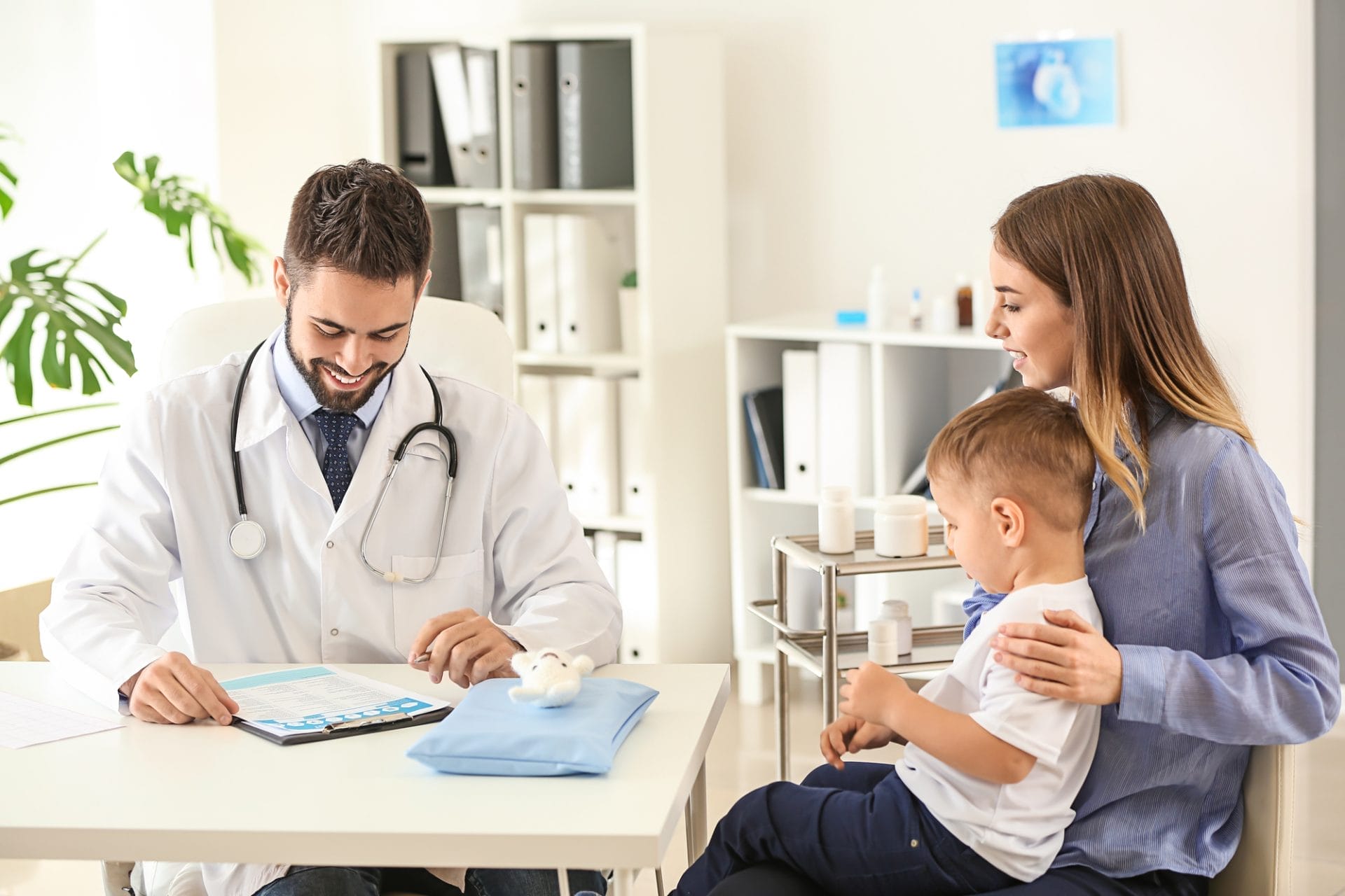 Una mujer y su hijo están sentados en una mesa con un médico hablando sobre atención pediátrica.