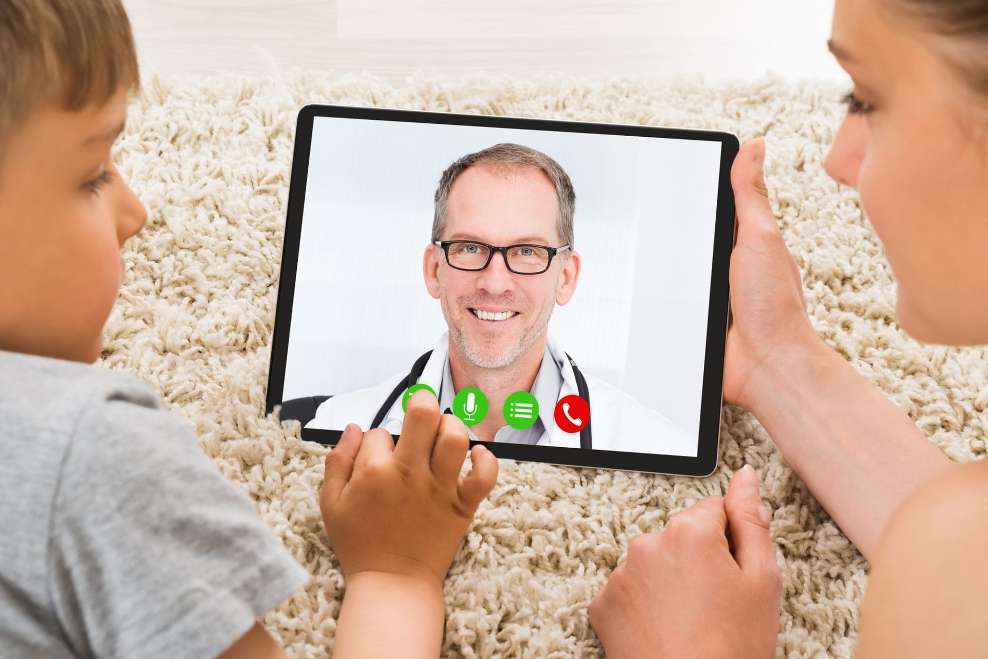 Una mujer y un niño miran una tableta con la cara de un médico, revolucionando la atención sanitaria a través de la telesalud.