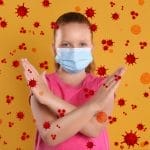 Una niña que lleva una máscara quirúrgica para protegerse contra enfermedades mortales, incluido el coronavirus, sobre un fondo amarillo.