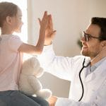 Un pediatra sonriente choca esos cinco con una niña que sostiene un osito de peluche en Bellaire, TX.