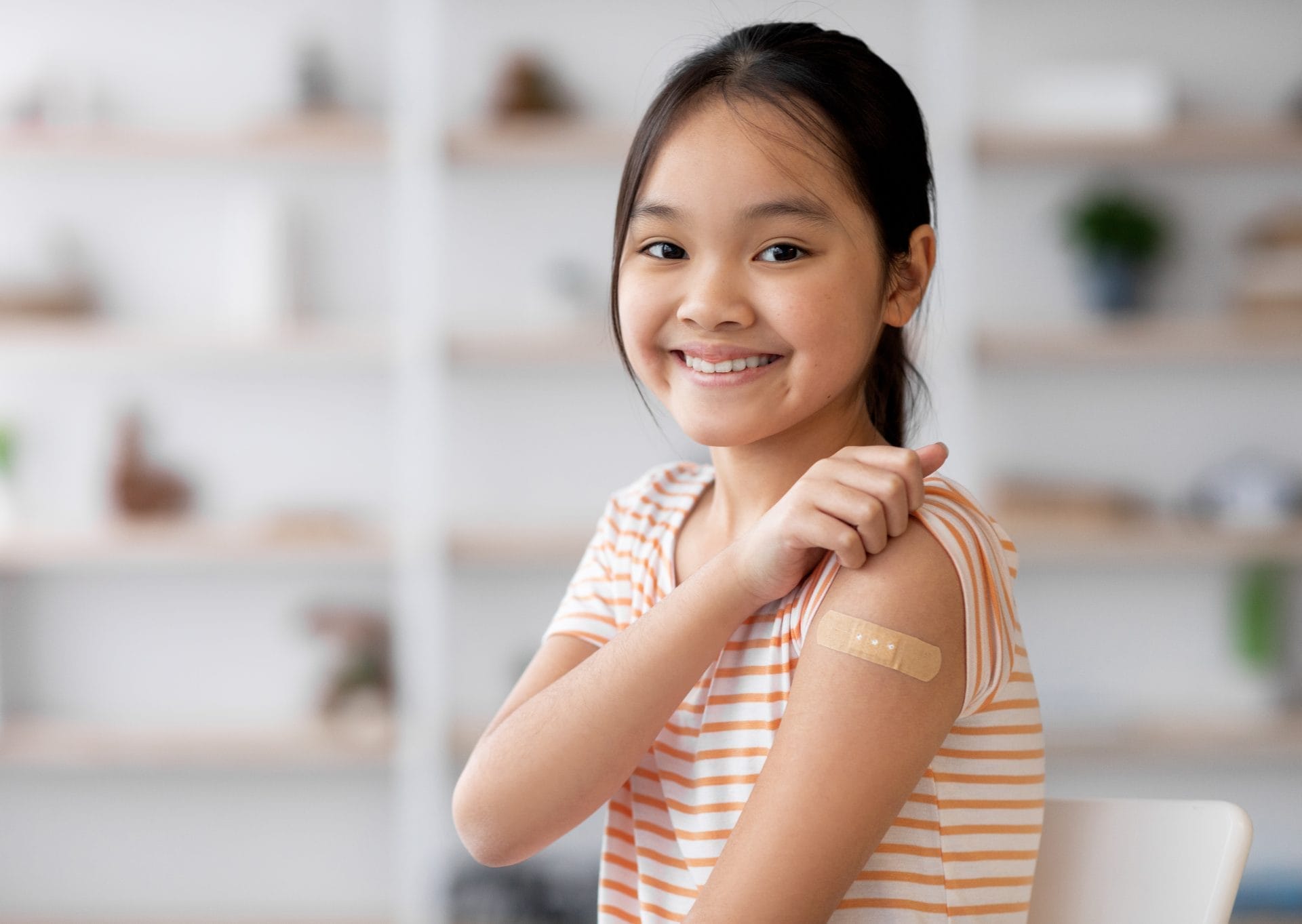 Una niña sonríe mientras muestra un vendaje en la parte superior de su brazo, lo que indica que recientemente recibió una vacuna.