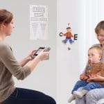 Un trabajador de la salud realiza una prueba ocular de detección temprana a un niño pequeño, que está sostenido por una mujer adulta, utilizando tecnología de detección de la visión digital en un entorno clínico.