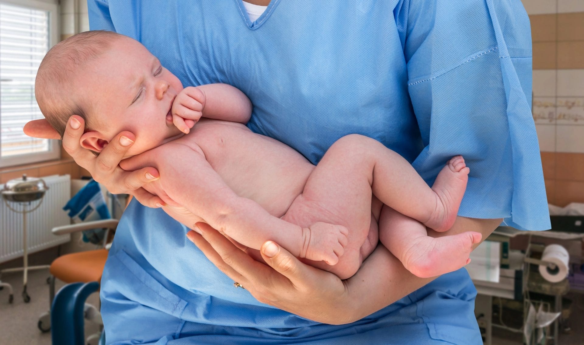 A newborn baby is being held by a doctor in a blue medical uniform, highlighting the expertise in newborn care, all within an indoor setting.