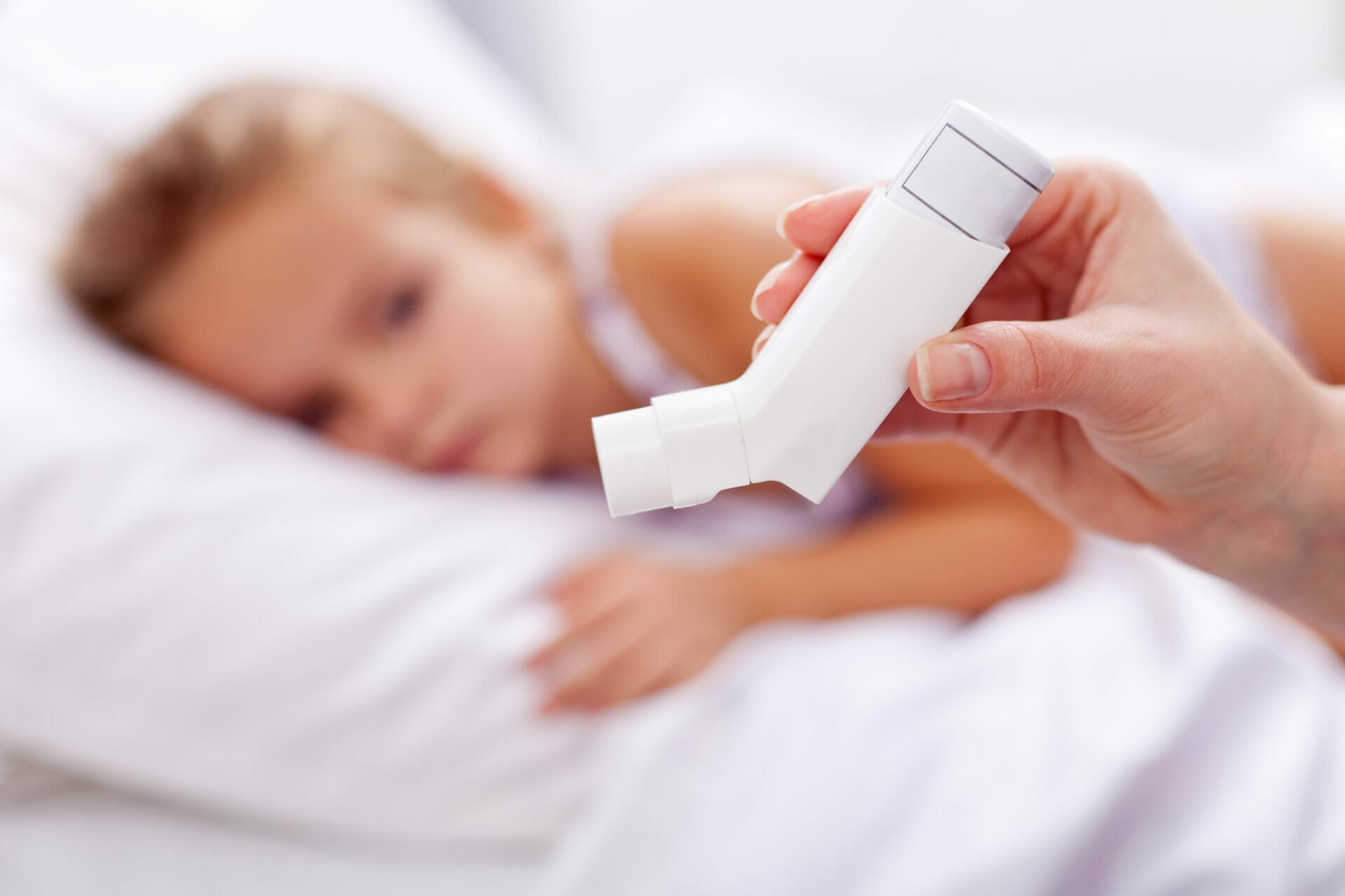 A person holds an inhaler in the foreground while a child lies in bed in the background, highlighting the importance of adolescent care.